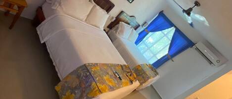 A hotel room with a bed, a desk, a ceiling fan, and a window with curtains.