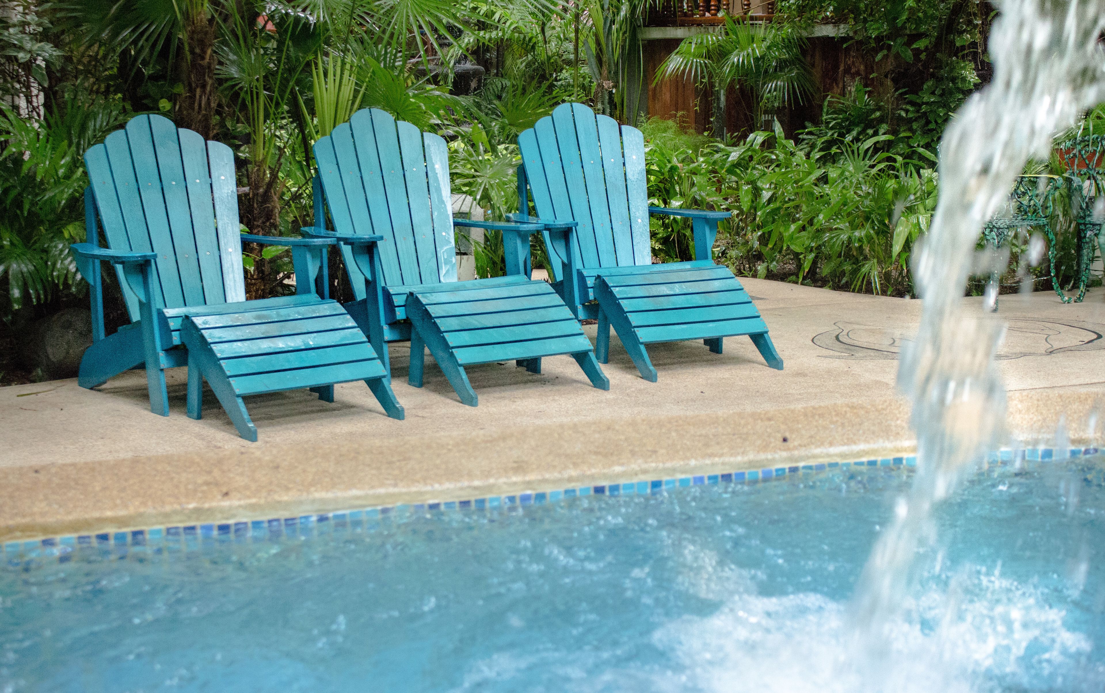 Tres sillas Adirondack azules junto a una piscina, con un elemento acuático en primer plano.