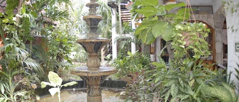 A multi-tiered stone fountain surrounded by lush greenery in an outdoor setting.