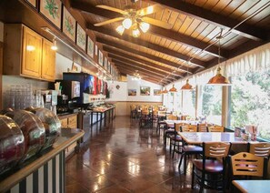 Un restaurante con vigas de madera en el techo, una zona de bufé y mesas de comedor con sillas.
