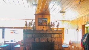 Un acogedor interior de cabaña con chimenea de piedra, techo de madera y zona de comedor con mesa y sillas.