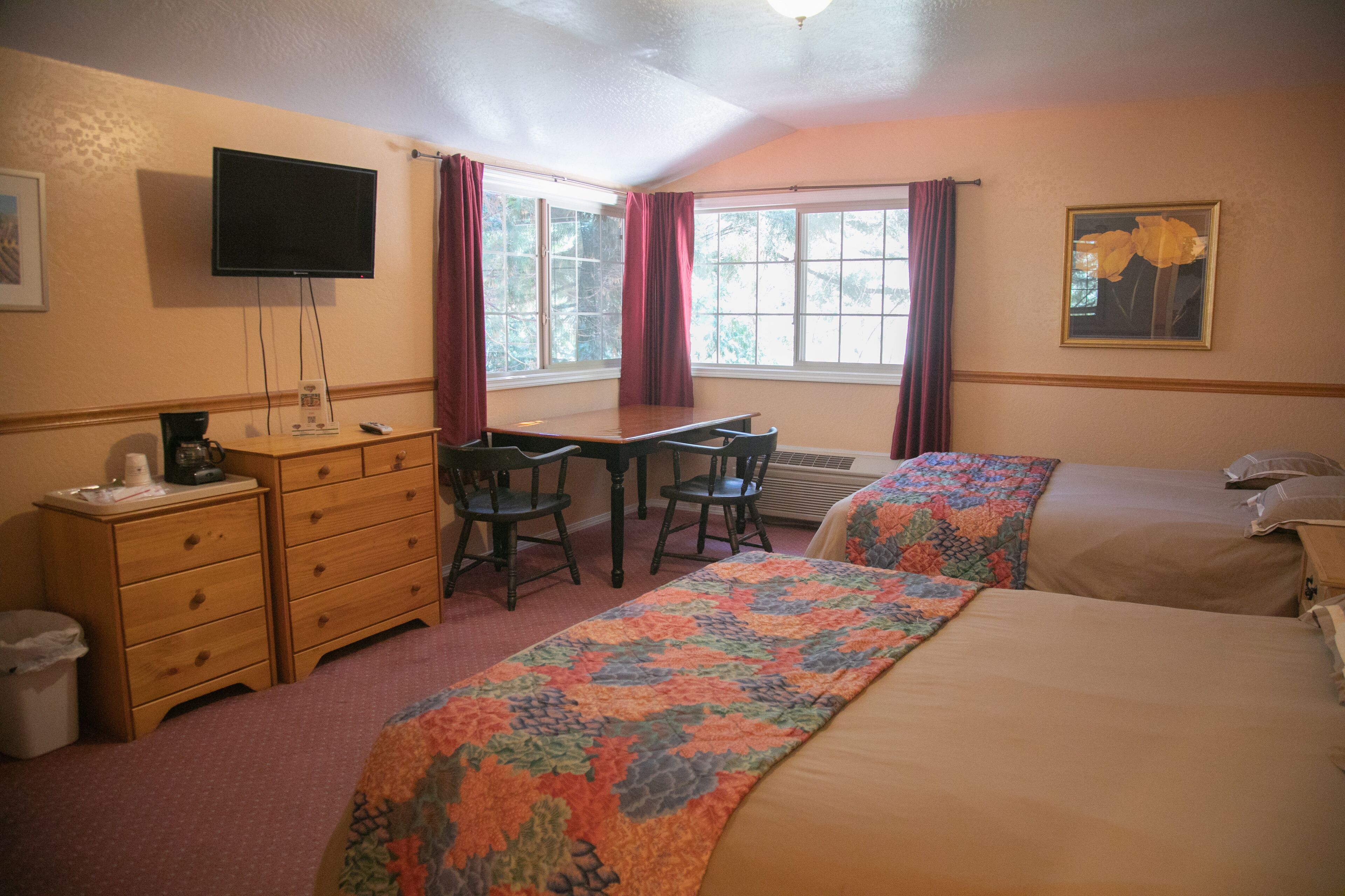 A hotel room with two beds, a desk, a chair, a television, and a window with curtains.