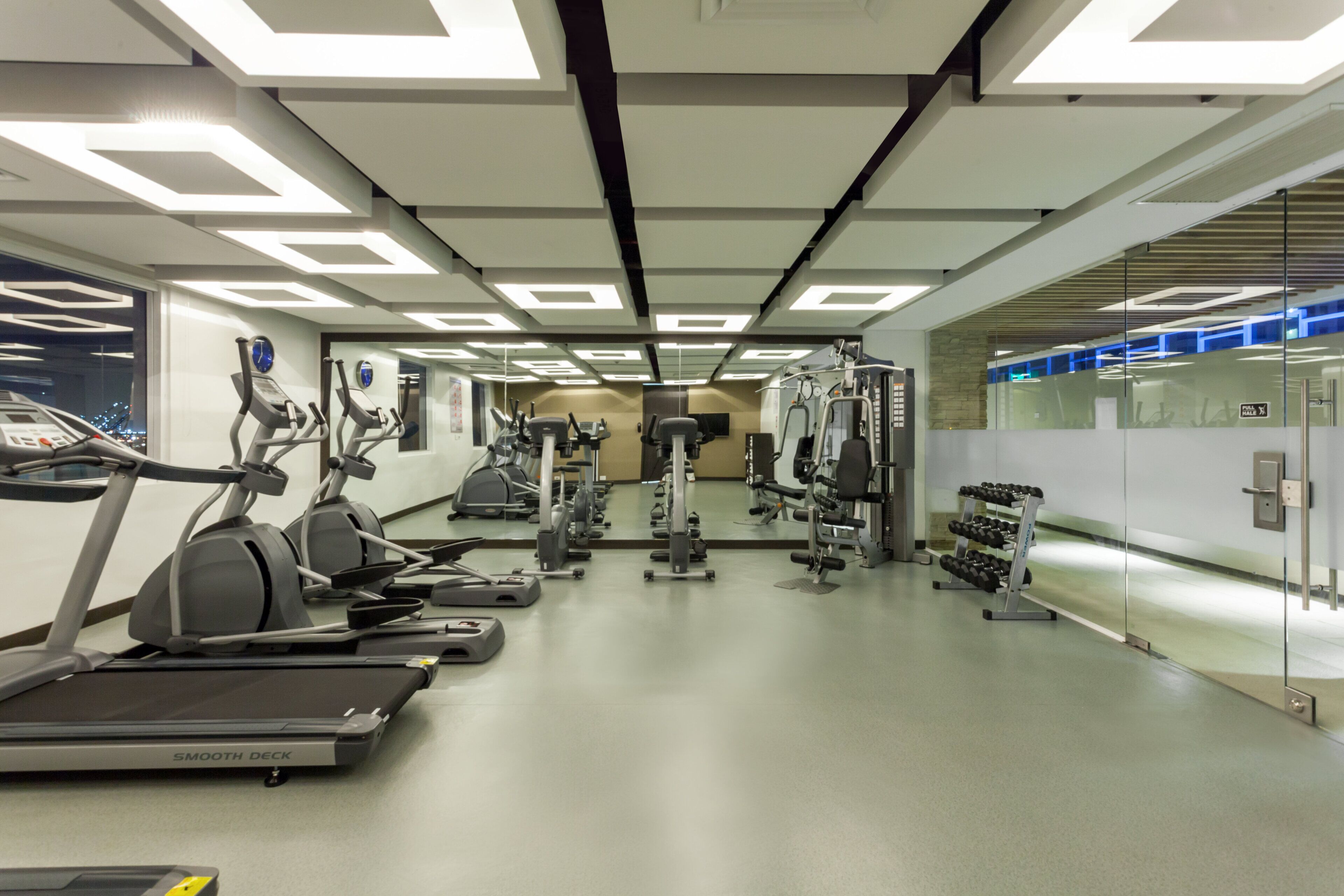 A modern gym with treadmills, elliptical machines, and weight equipment.