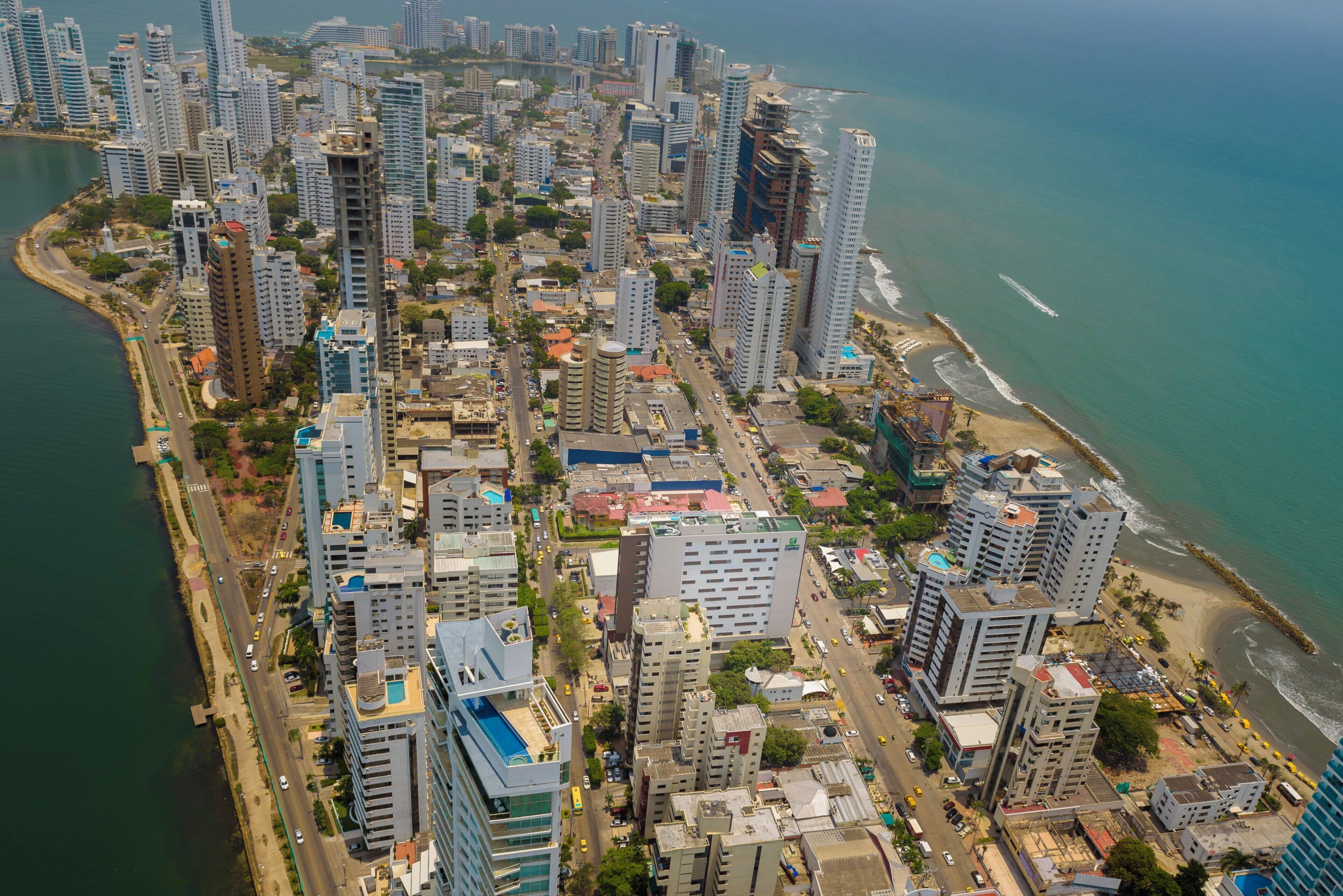 Un paisaje urbano costero con edificios altos, una playa y un puerto deportivo.