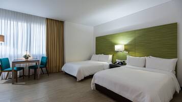 Une chambre d’hôtel avec deux lits, un bureau avec des chaises, une lampe et une tête de lit verte.
