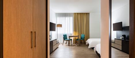 Une chambre d’hôtel avec une armoire en bois, un lit, un bureau avec une lampe, deux chaises et un téléviseur.