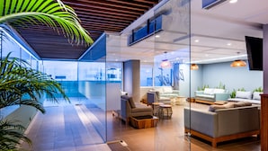 A modern hotel lobby with glass walls, comfortable seating, and a pool area.