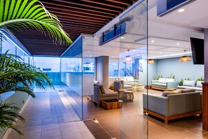 A modern hotel lobby with glass walls, comfortable seating, and a pool area.
