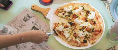 A pizza on a plate with a pizza cutter, a glass of drink, and a menu on a table.