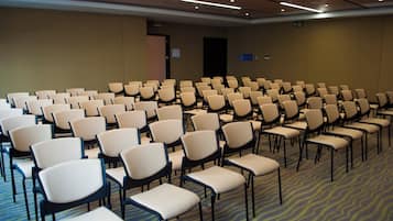 Un salón de conferencias con filas de sillas, piso alfombrado y una puerta al fondo.