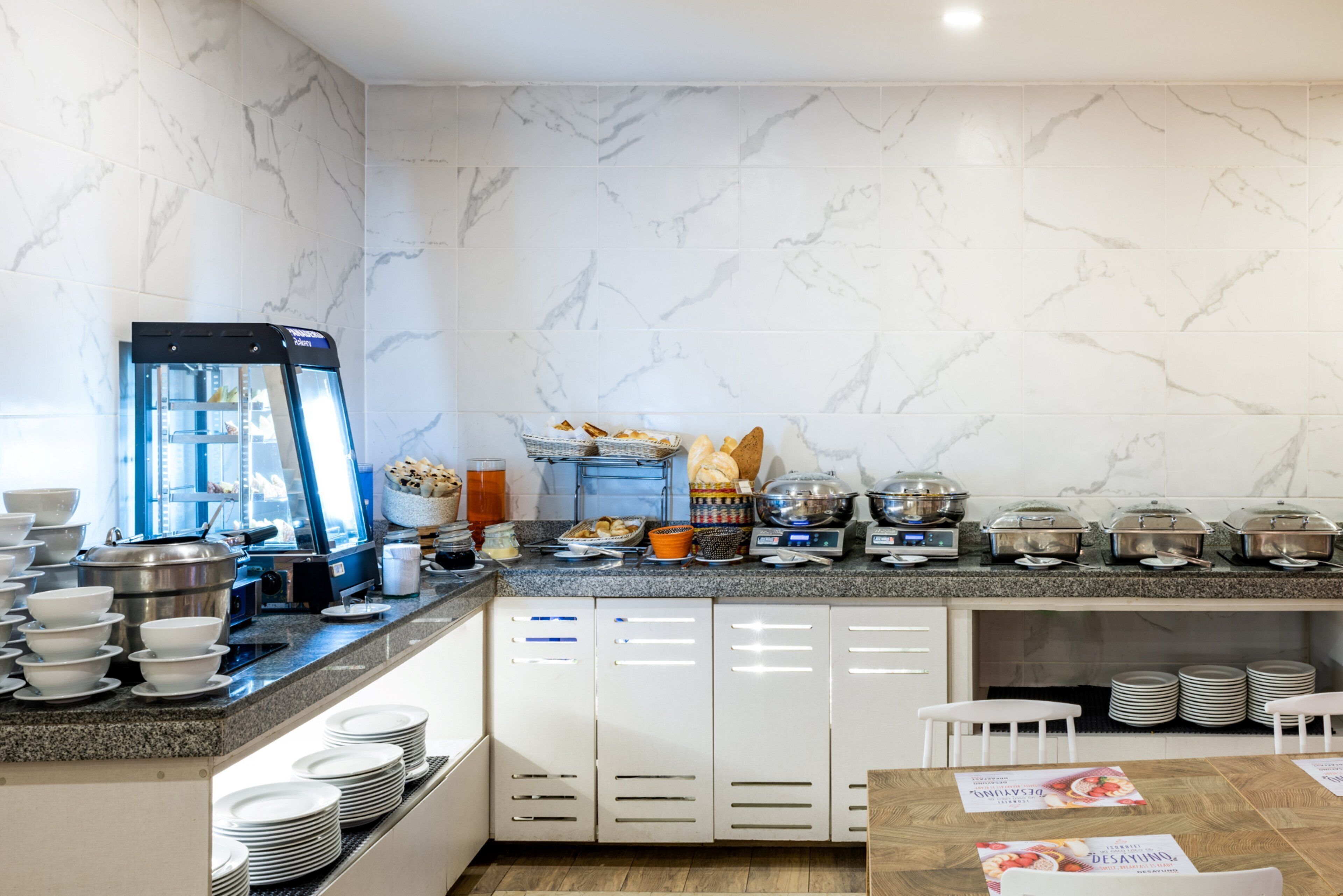 A modern hotel kitchen with marble walls, a buffet setup, and a coffee machine.
