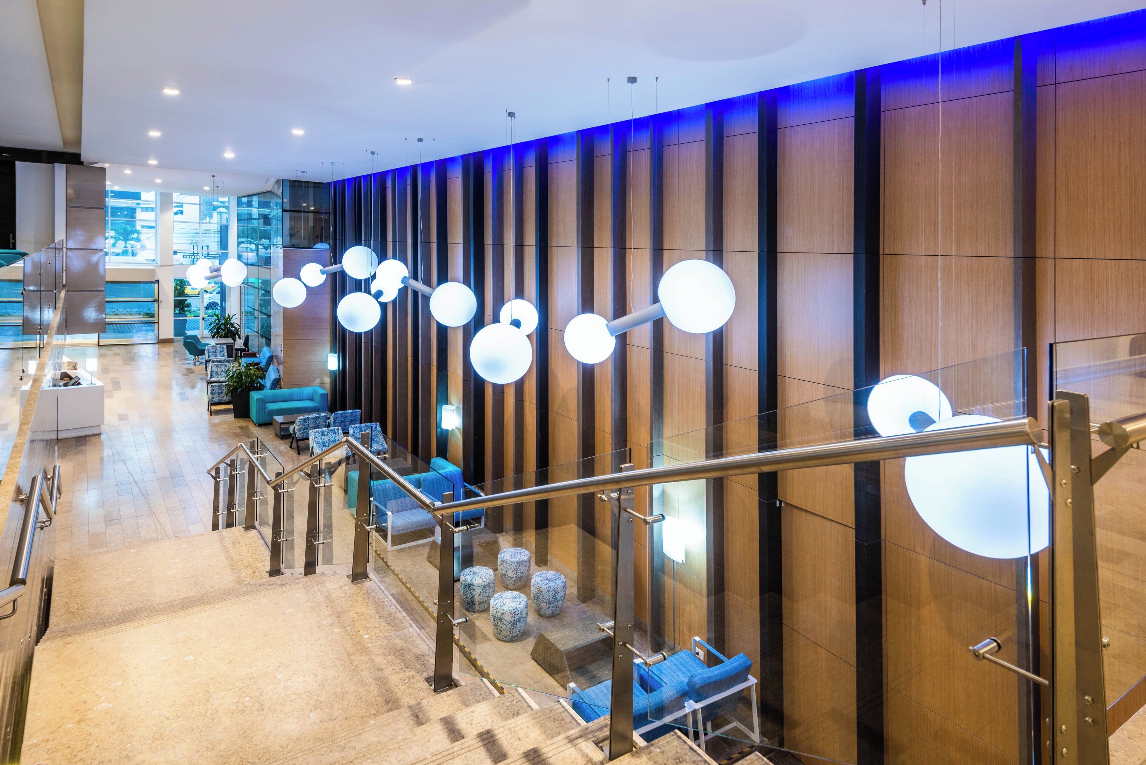 A modern hotel lobby with a staircase, seating area, and a view of the outside.