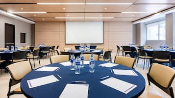 Une salle de conférence équipée de tables rondes, de chaises, de bouteilles d’eau et d’écrans de présentation.