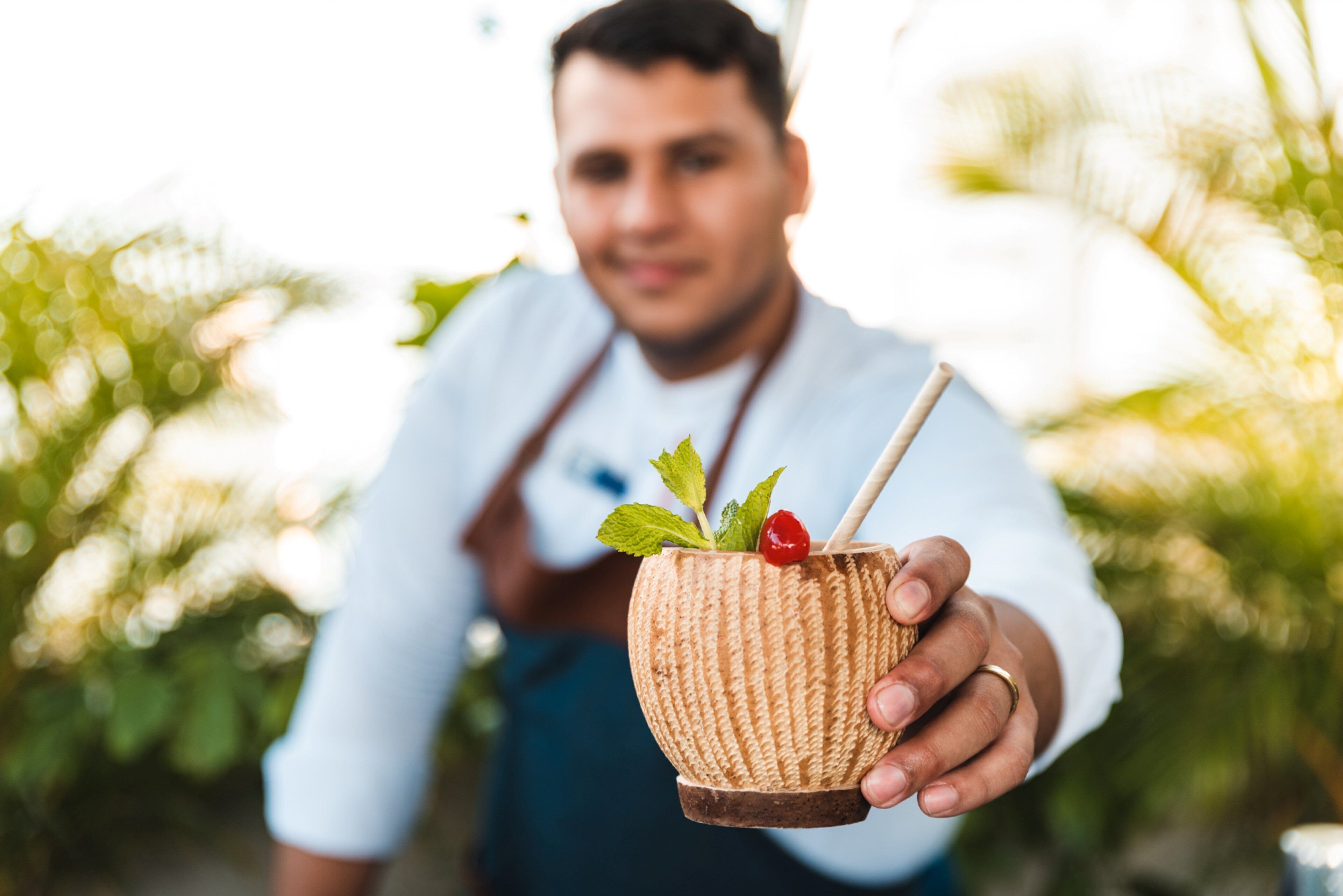 A person holding a textured drink cup with a straw and a cherry garnish.