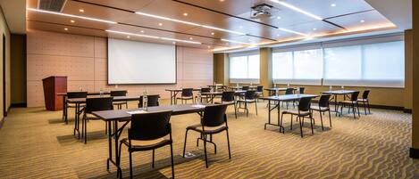 A conference room with tables, chairs, a projector screen, and a carpeted floor.