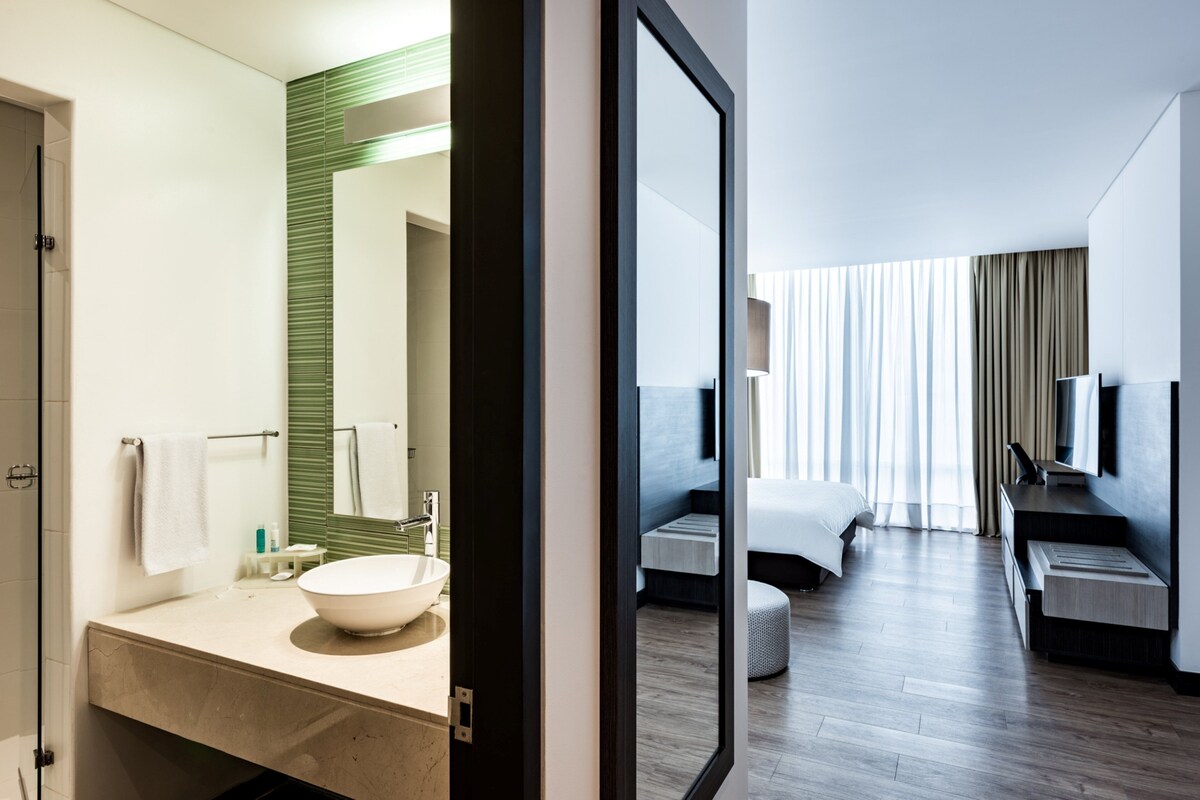 A modern hotel bathroom with a large mirror, a white sink, and a towel rack.