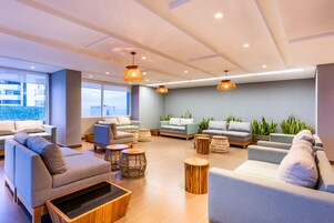 A modern lounge area with sofas, round wooden tables, and hanging wicker lamps.