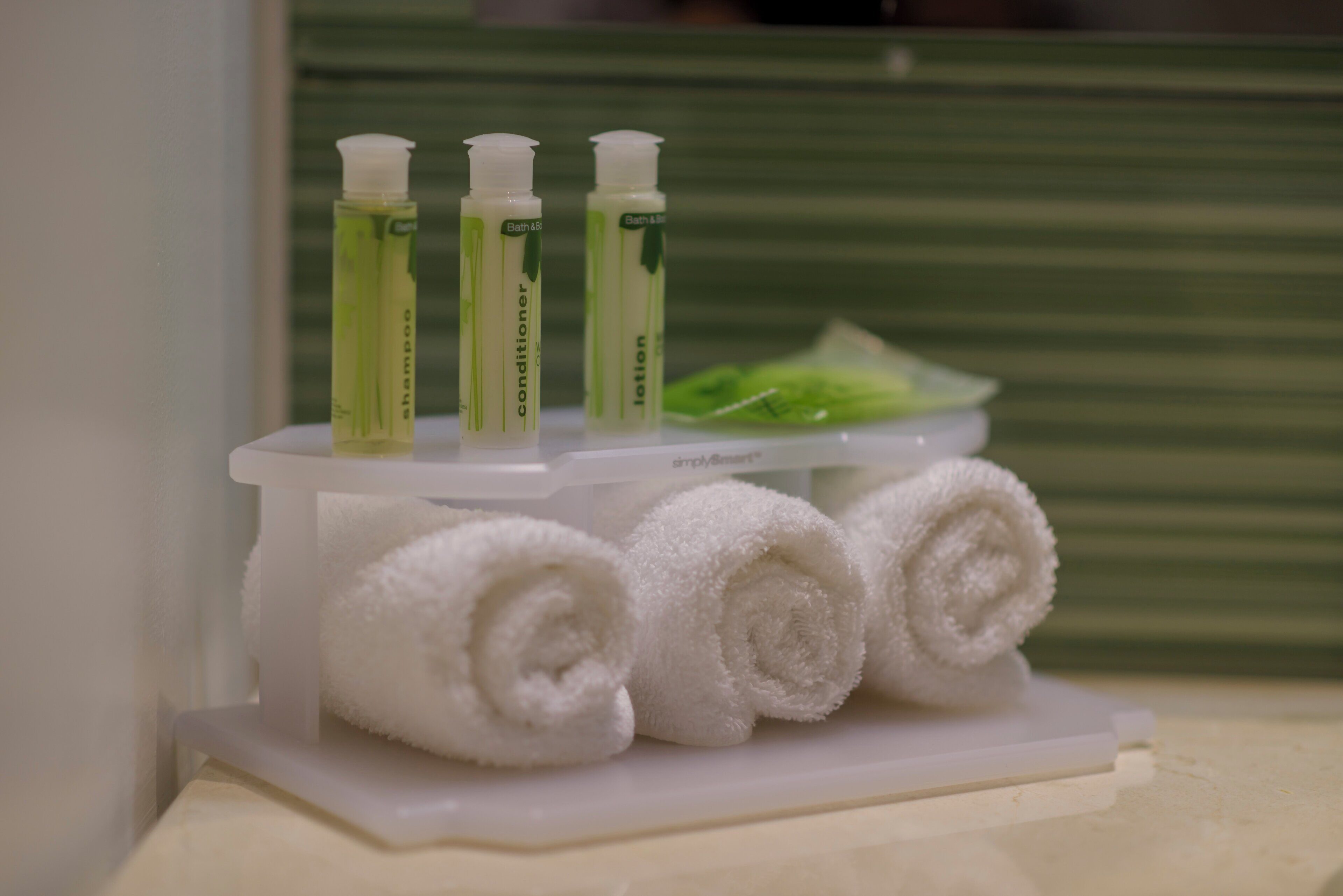 A bathroom with a white towel rack holding three rolled towels and a bottle of green liquid soap.