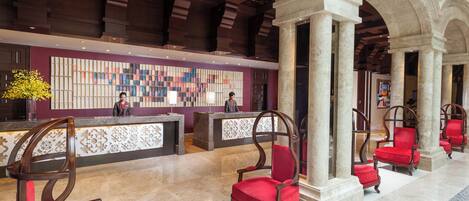 A hotel lobby with a reception desk, red upholstered chairs, and a decorative wall.