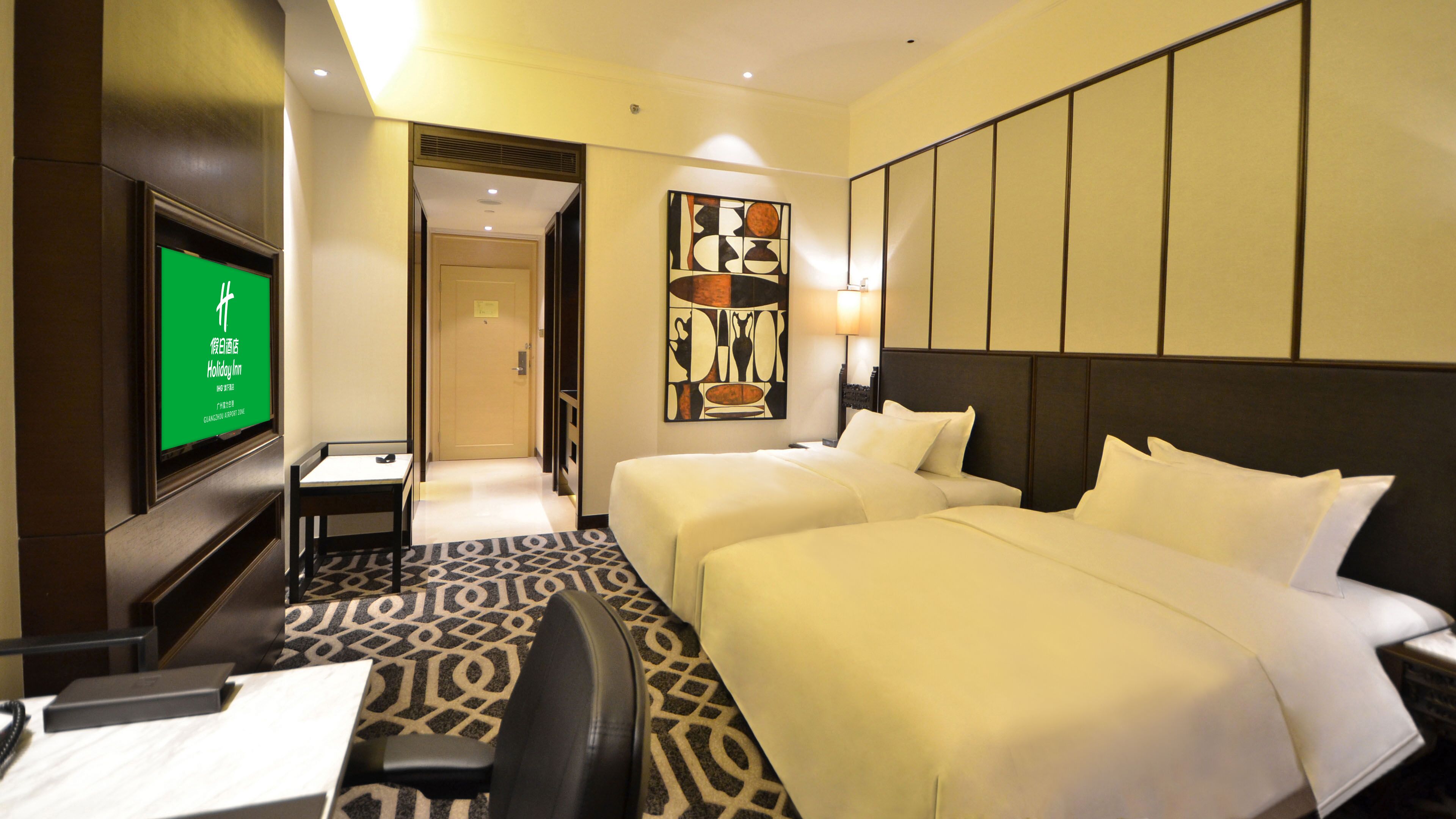 A hotel room with two beds, a desk, a chair, a TV, and a painting on the wall.