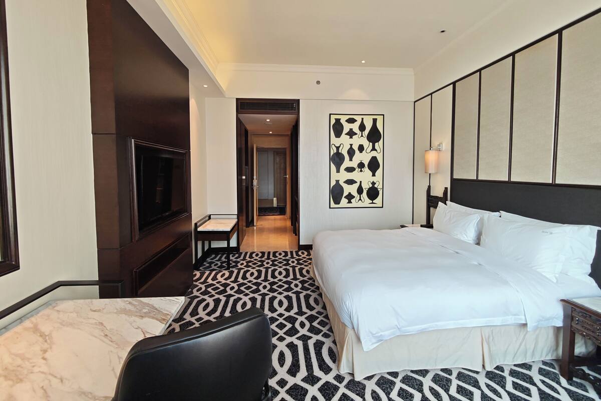 A hotel room with a large bed, a television, a patterned floor, and a wall-mounted artwork.