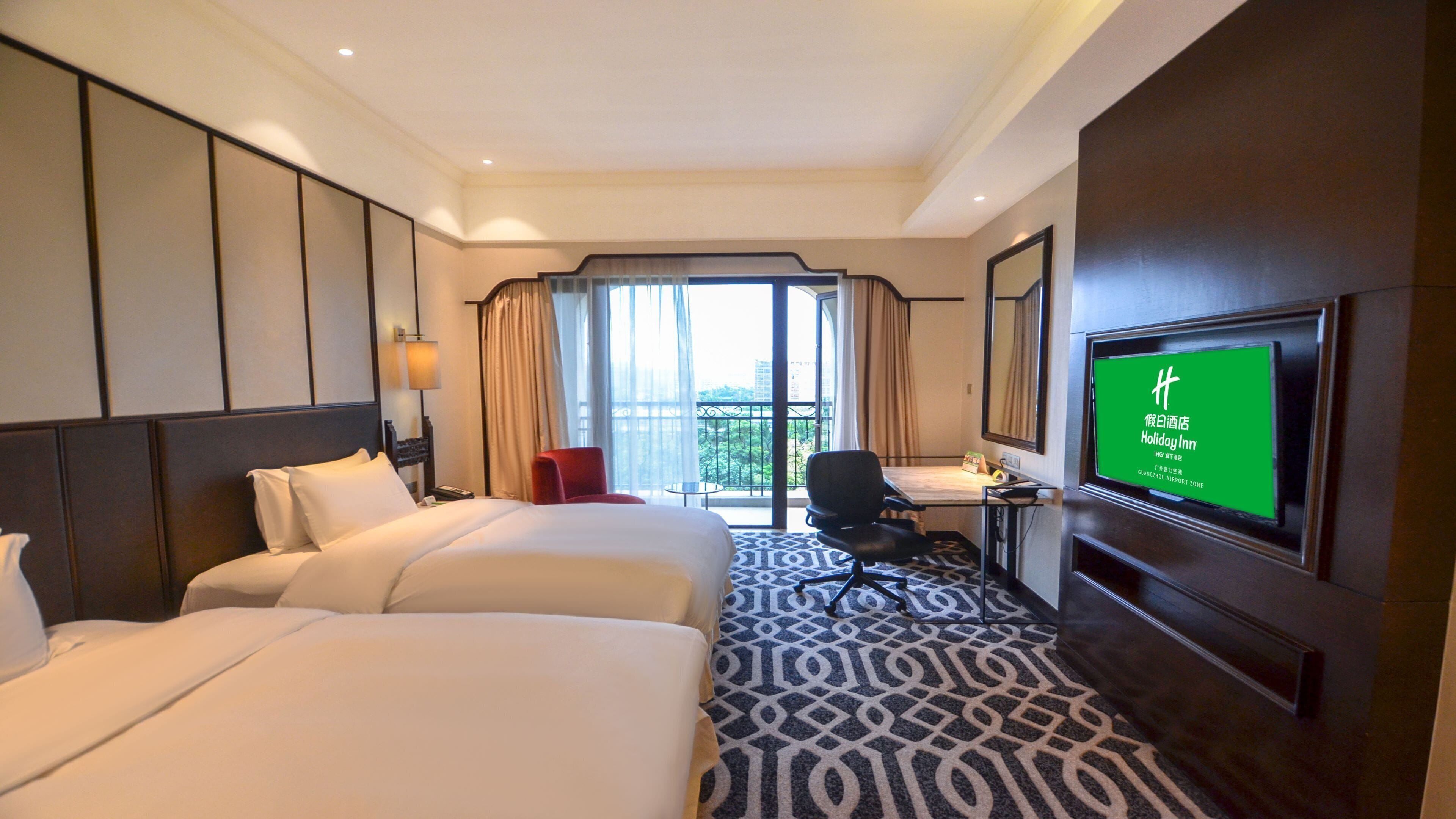 Habitación de hotel con dos camas, un escritorio, una silla, un televisor y vistas al exterior.