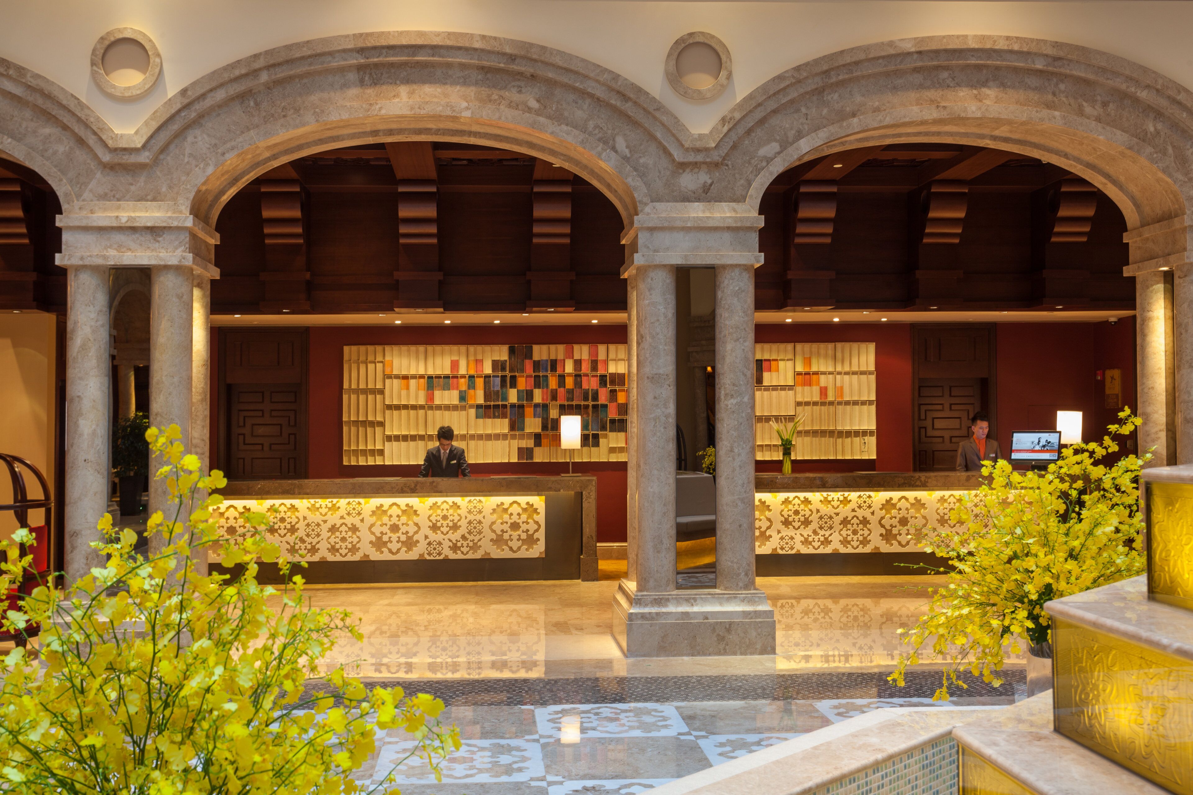 Zona de recepción con mostrador de entrada, dos recepcionistas y una pared decorativa con azulejos estampados.