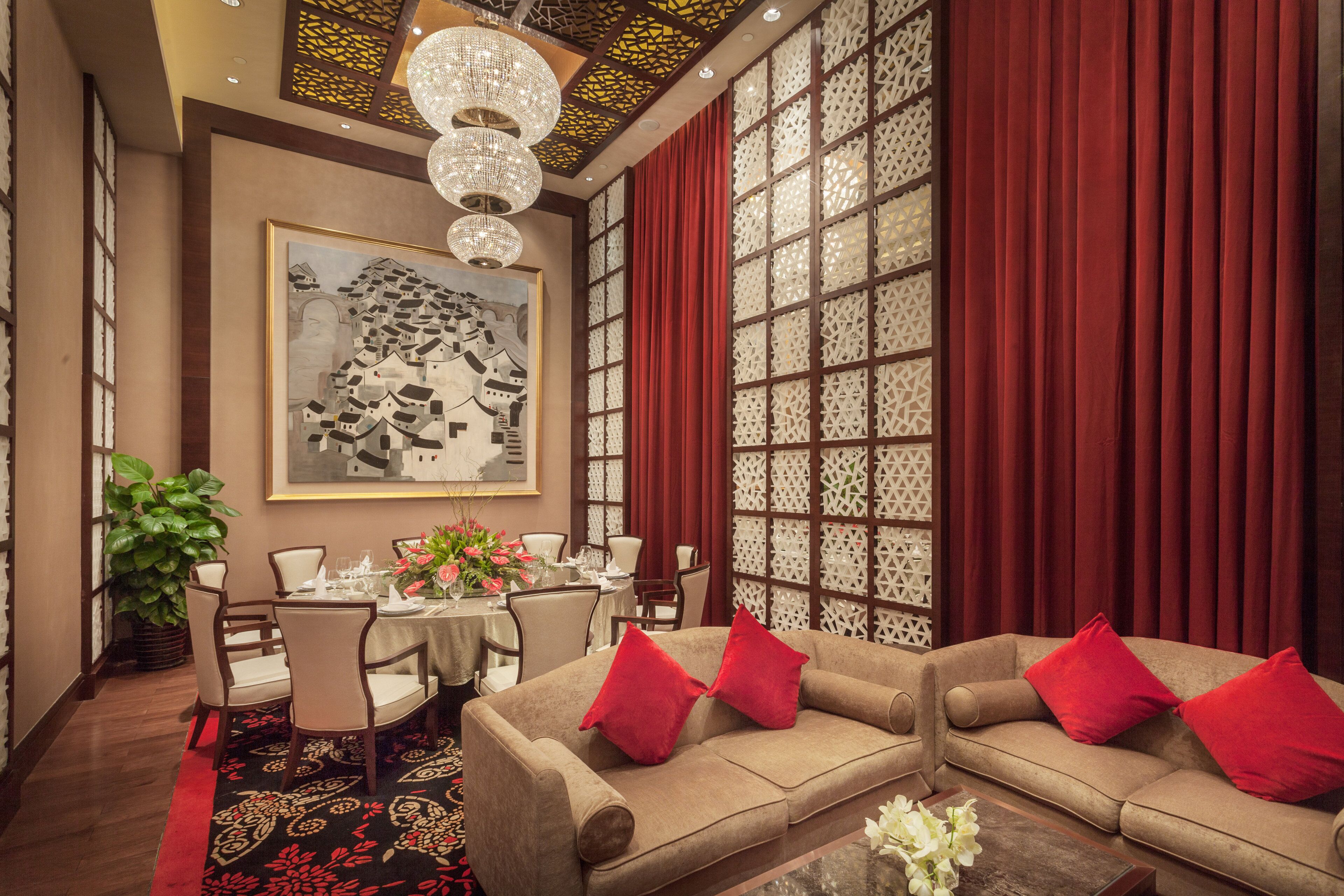 Une chambre d’hôtel comprenant un coin repas, un ensemble de canapés et une grande fenêtre avec des rideaux rouges.