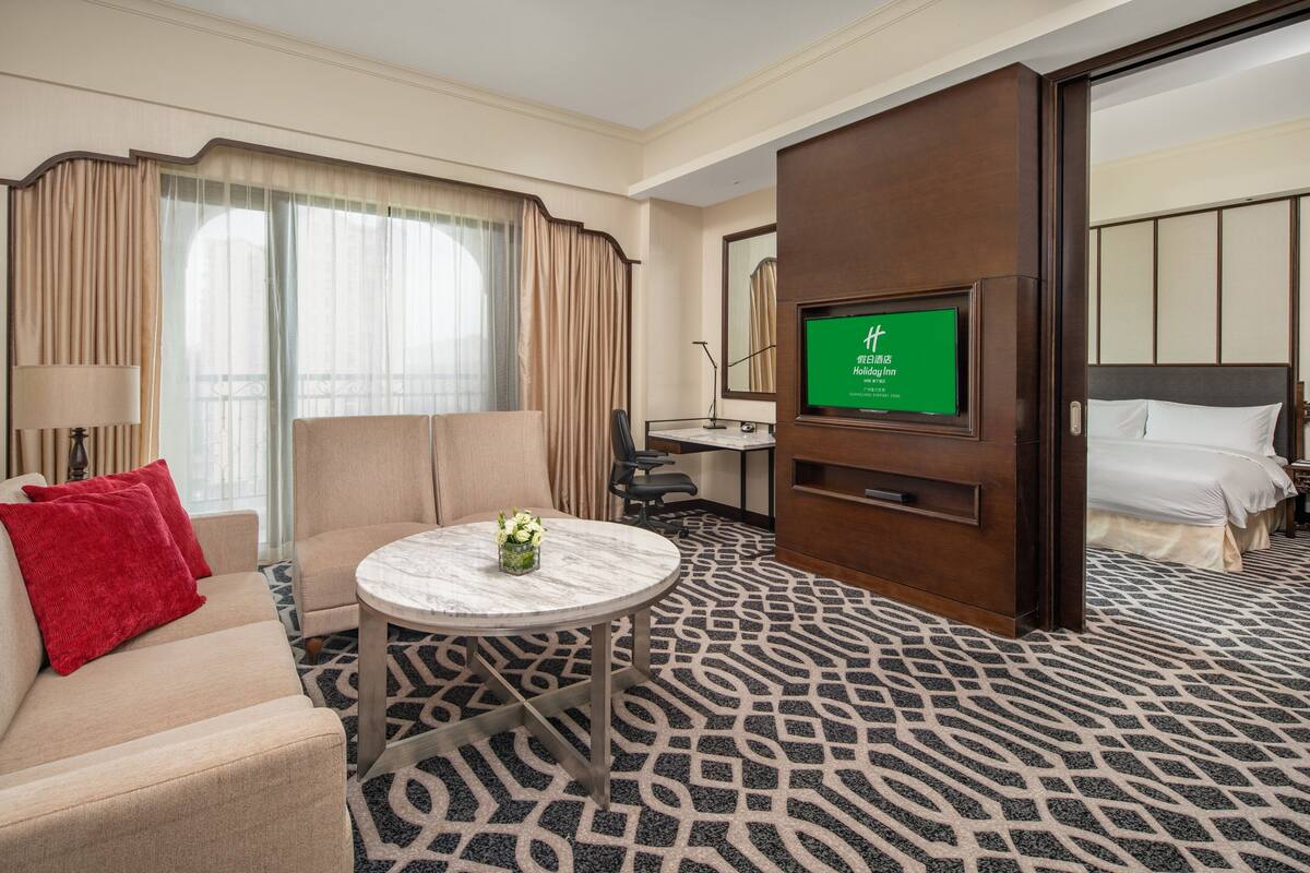 A hotel room with a bed, a TV, a desk, a chair, and a small table with a vase of flowers.