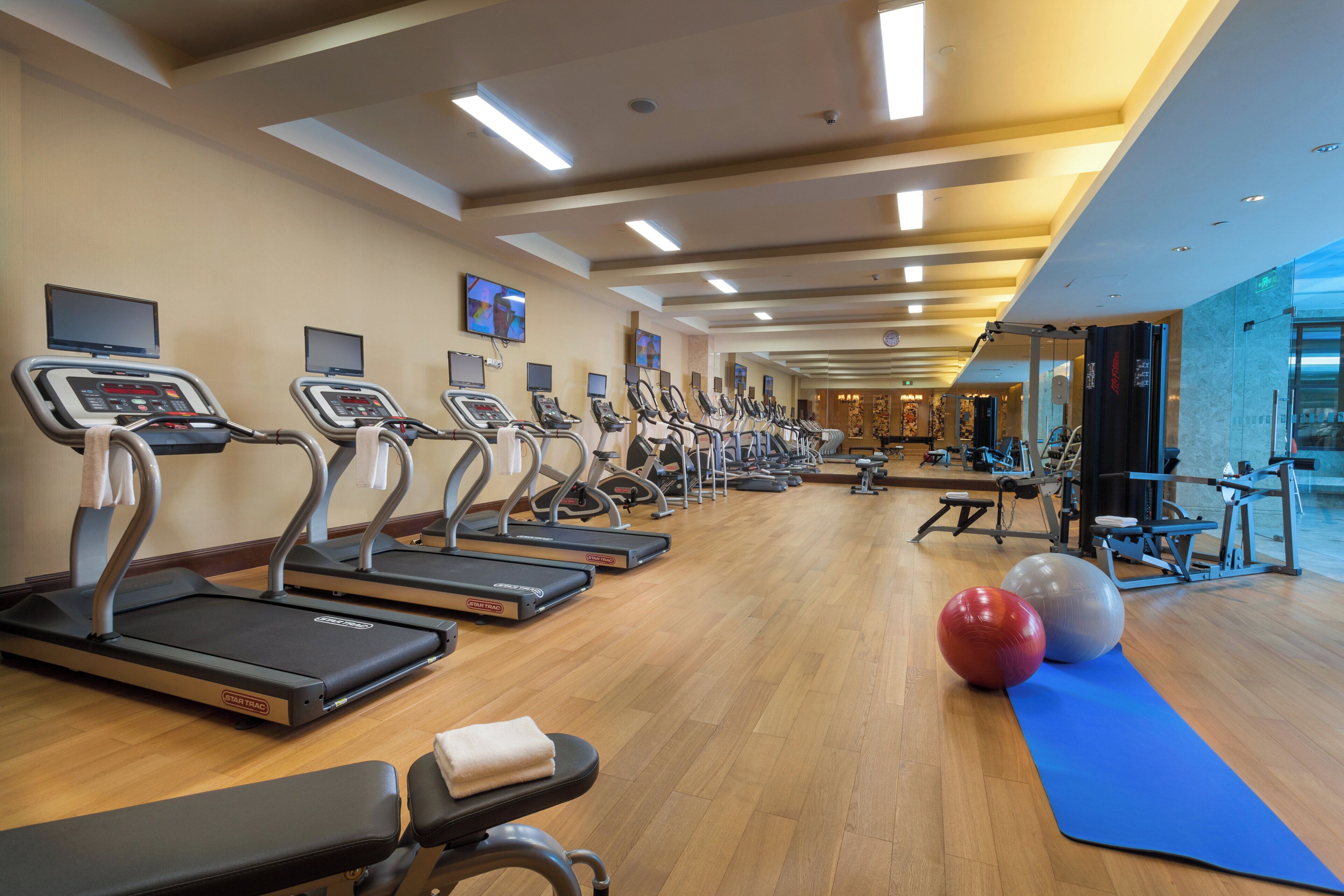A gym with multiple treadmills, exercise balls, and a blue mat.