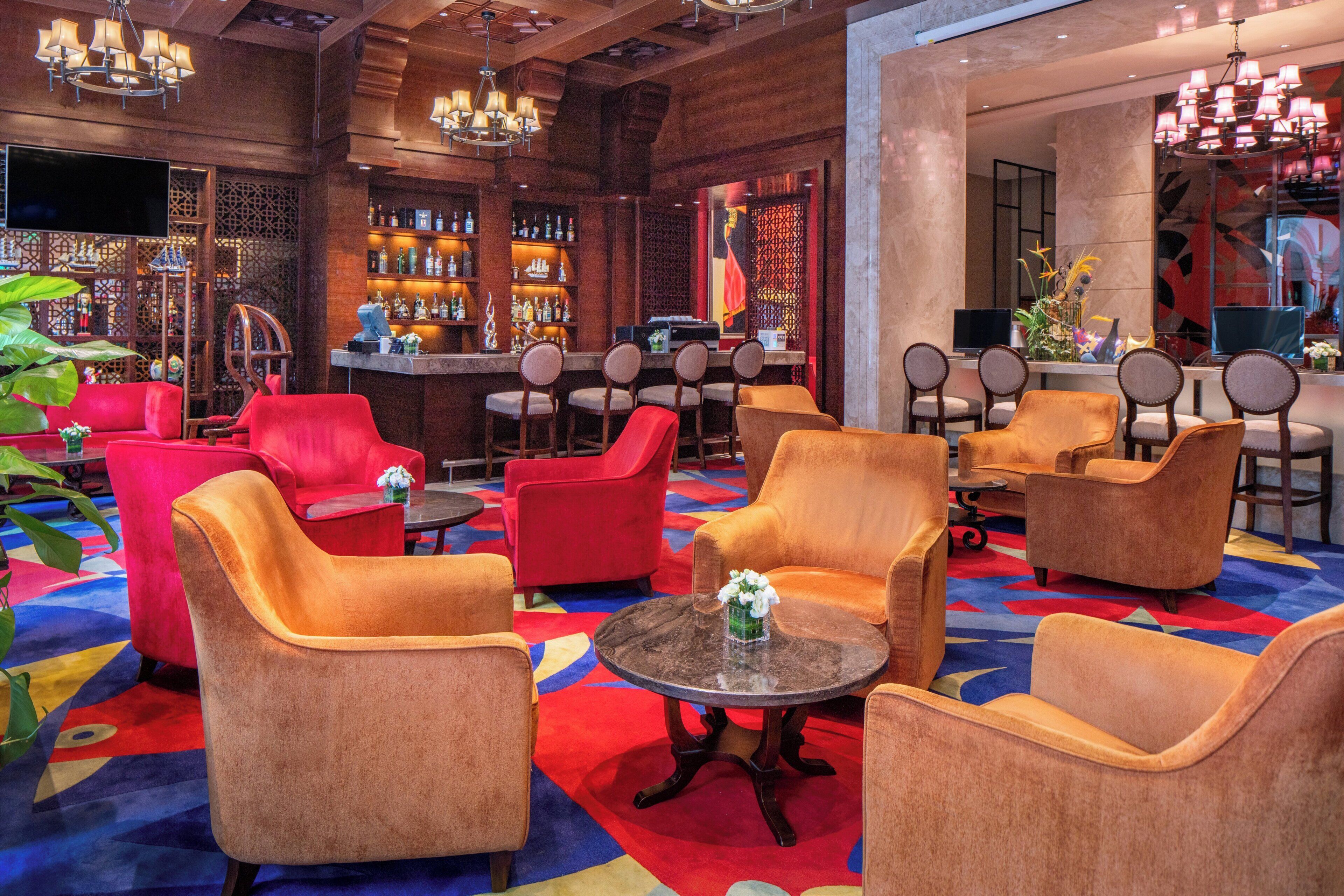 Un hall d’hôtel doté de plusieurs espaces aménagés avec des sièges, d’un bar et d’un mur décoratif.