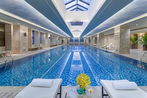 A large indoor swimming pool with a clear view of the ceiling and walls, surrounded by lounge chairs and a flower arrangement. - Holiday Inn Airport Guangzhou by IHG (Guangzhou)