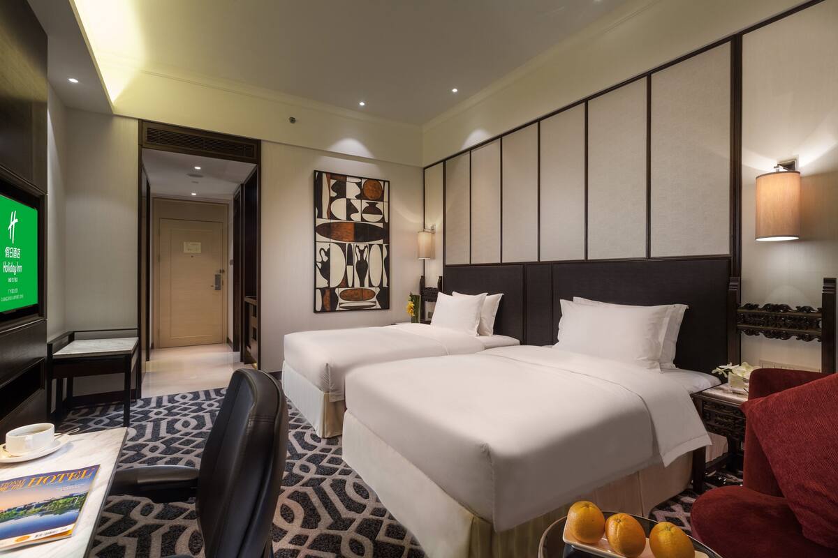 A hotel room with two beds, a desk, a chair, a TV, and a decorative wall piece.