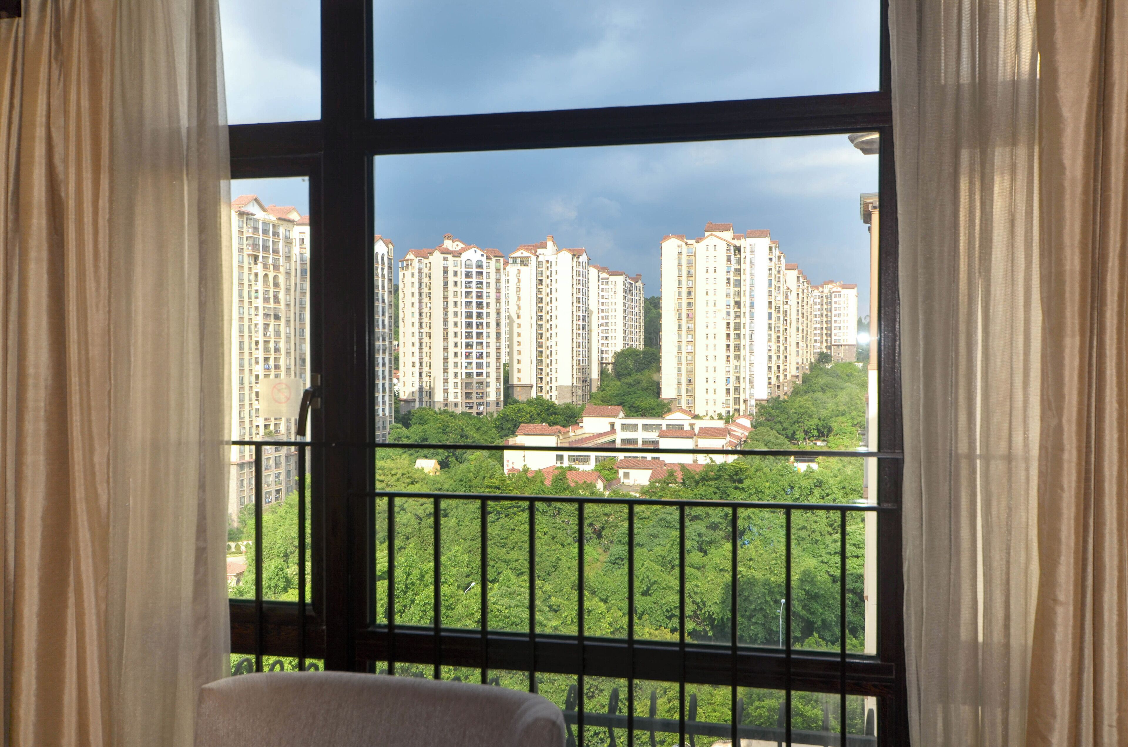A room with a large window overlooking high-rise residential buildings and a green park.