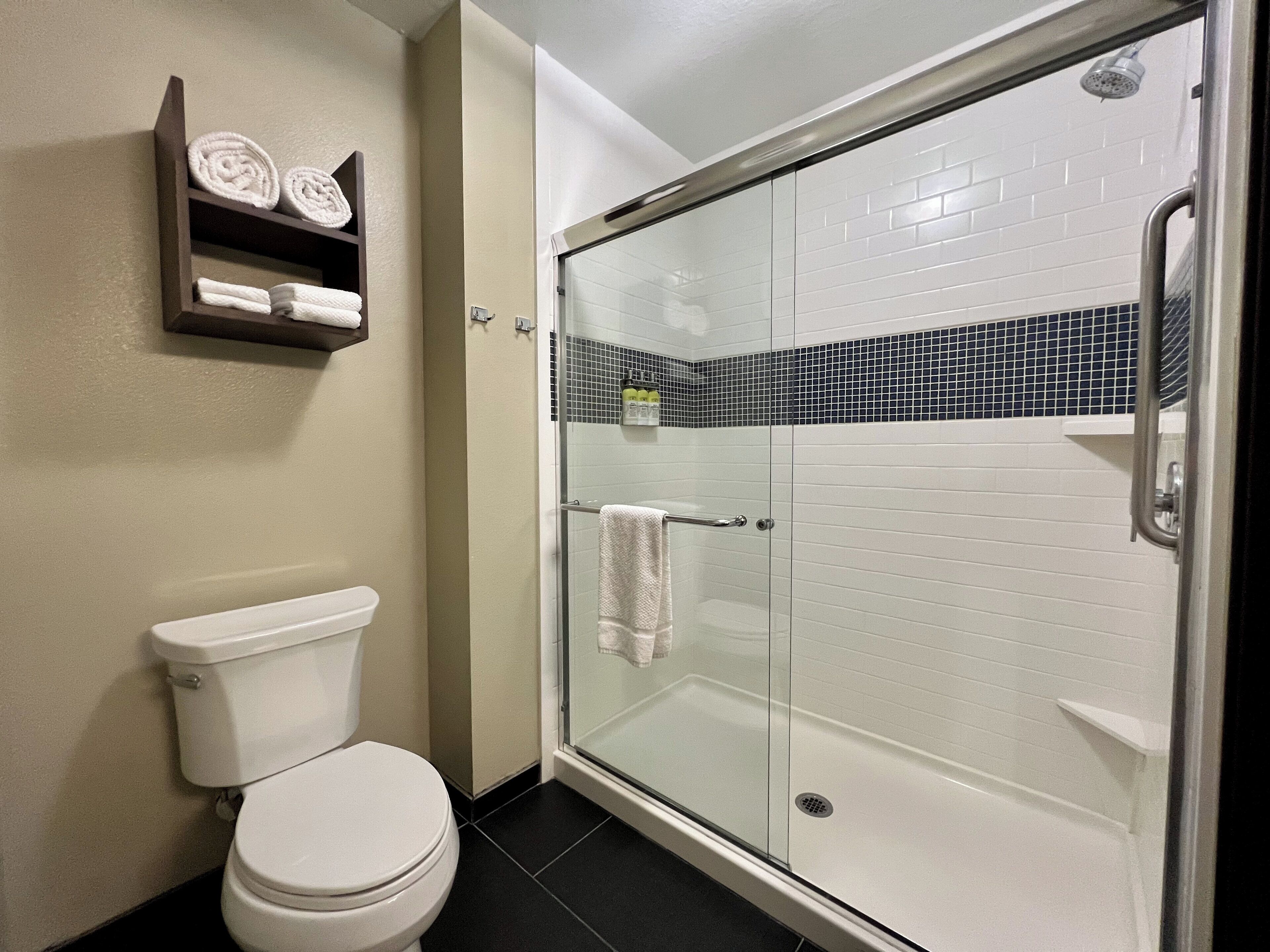 Une salle de bain moderne avec une douche à parois de verre, des toilettes et une étagère où sont rangées les serviettes.