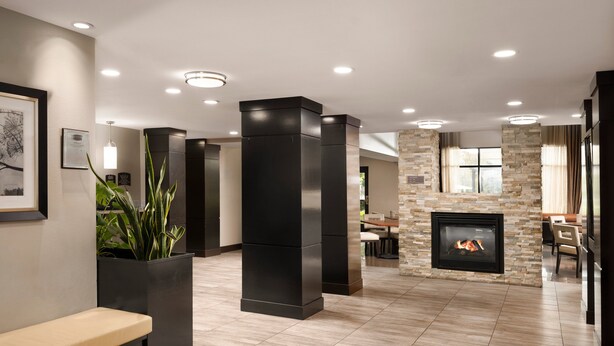 A modern lobby with a stone fireplace, black pillars, and a wooden bench. - Staybridge Suites Carlsbad by IHG (Carlsbad)