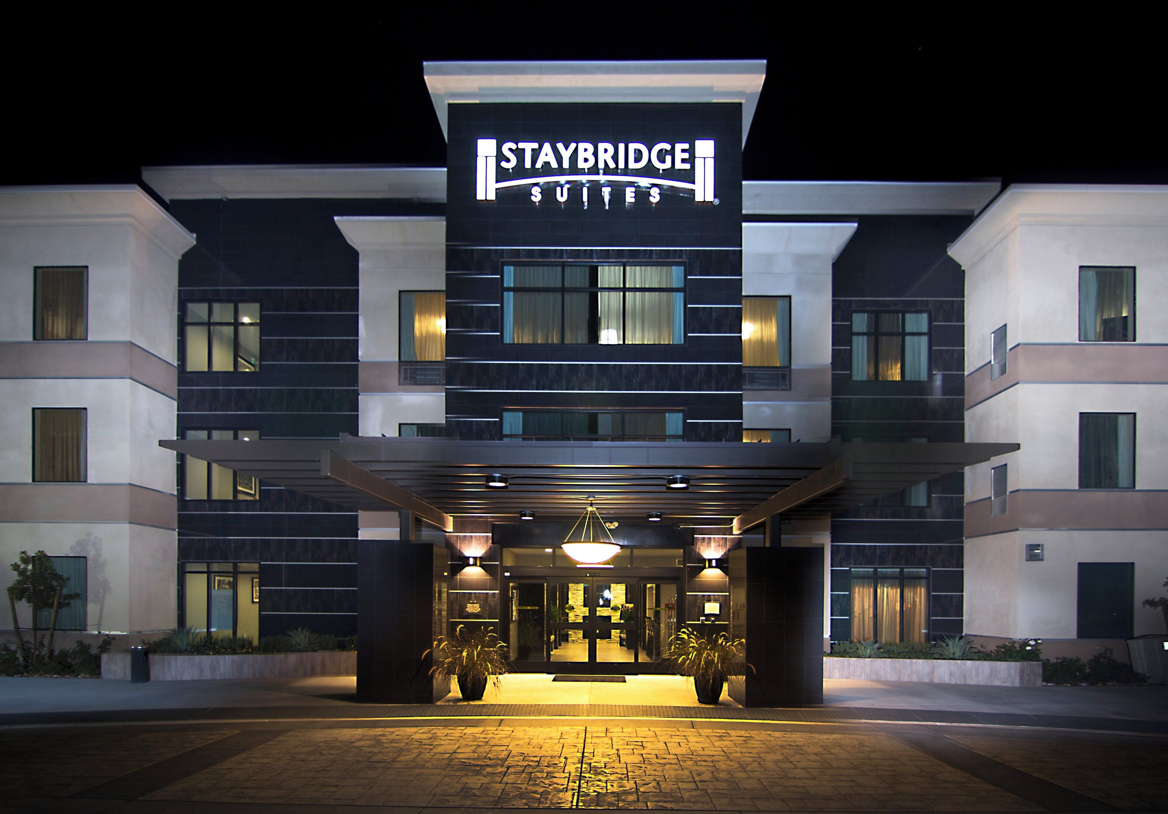 L’entrée d’un hôtel Staybridge Suites, de nuit, avec un design moderne, une enseigne lumineuse et une entrée accueillante.
