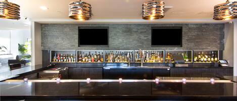 A bar area with a long counter, multiple seating options, and hanging pendant lights.