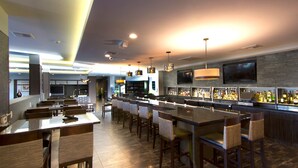 A modern bar area with a long counter, multiple seating options, and a large flat-screen TV mounted on the wall. - Staybridge Suites Carlsbad by IHG (Carlsbad)