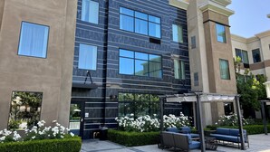 A modern building with multiple windows and a covered outdoor seating area with blue furniture. - Staybridge Suites Carlsbad by IHG (Carlsbad)