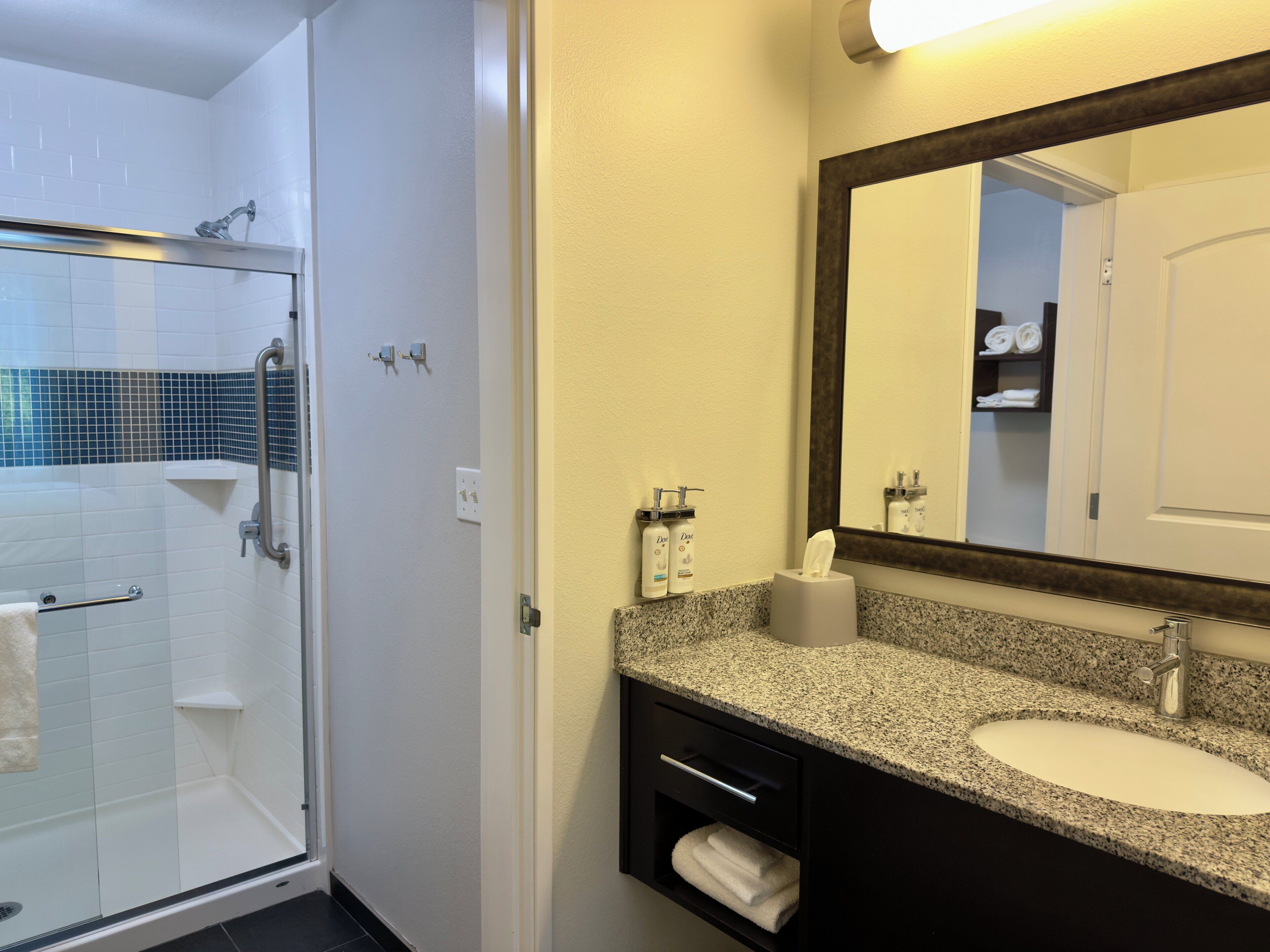 A bathroom with a glass shower enclosure, a sink with a granite countertop, and a mirror above the sink.