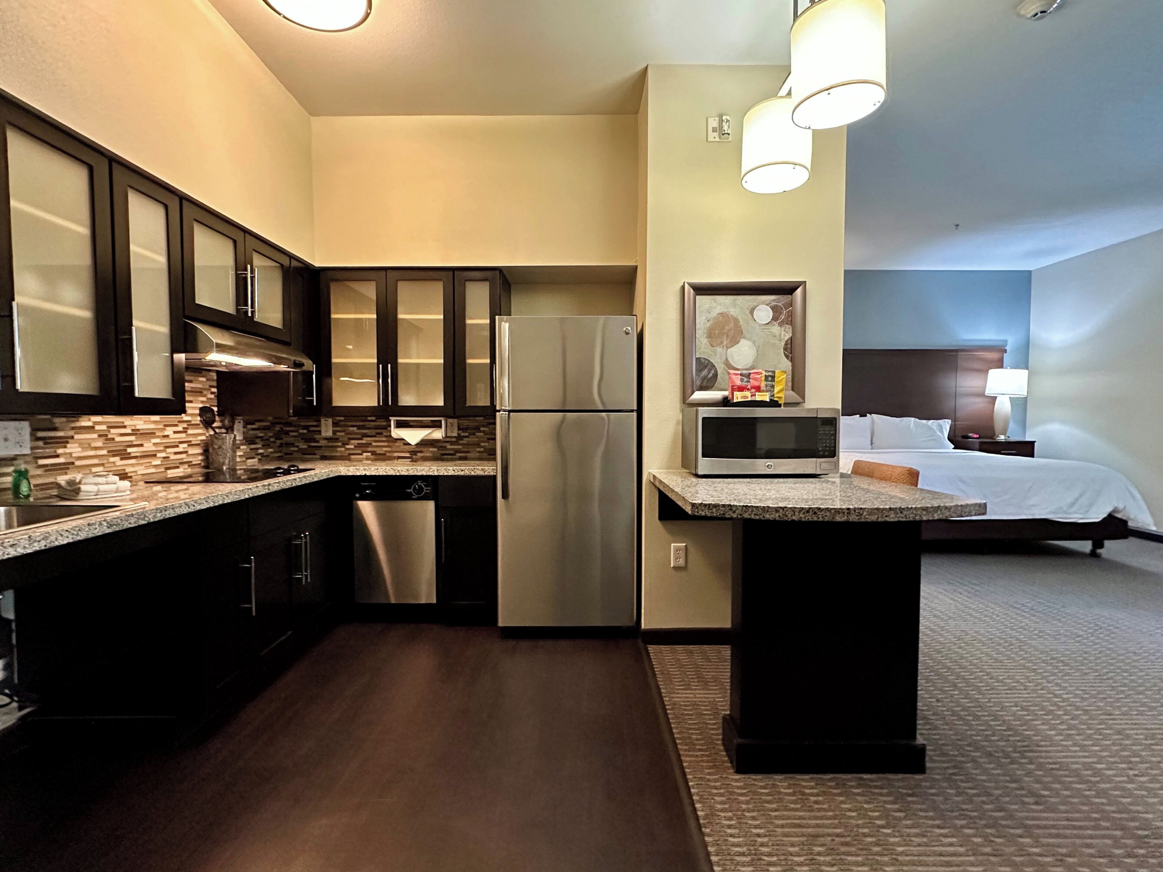 A compact hotel room with a kitchenette, a bed, and a bathroom.