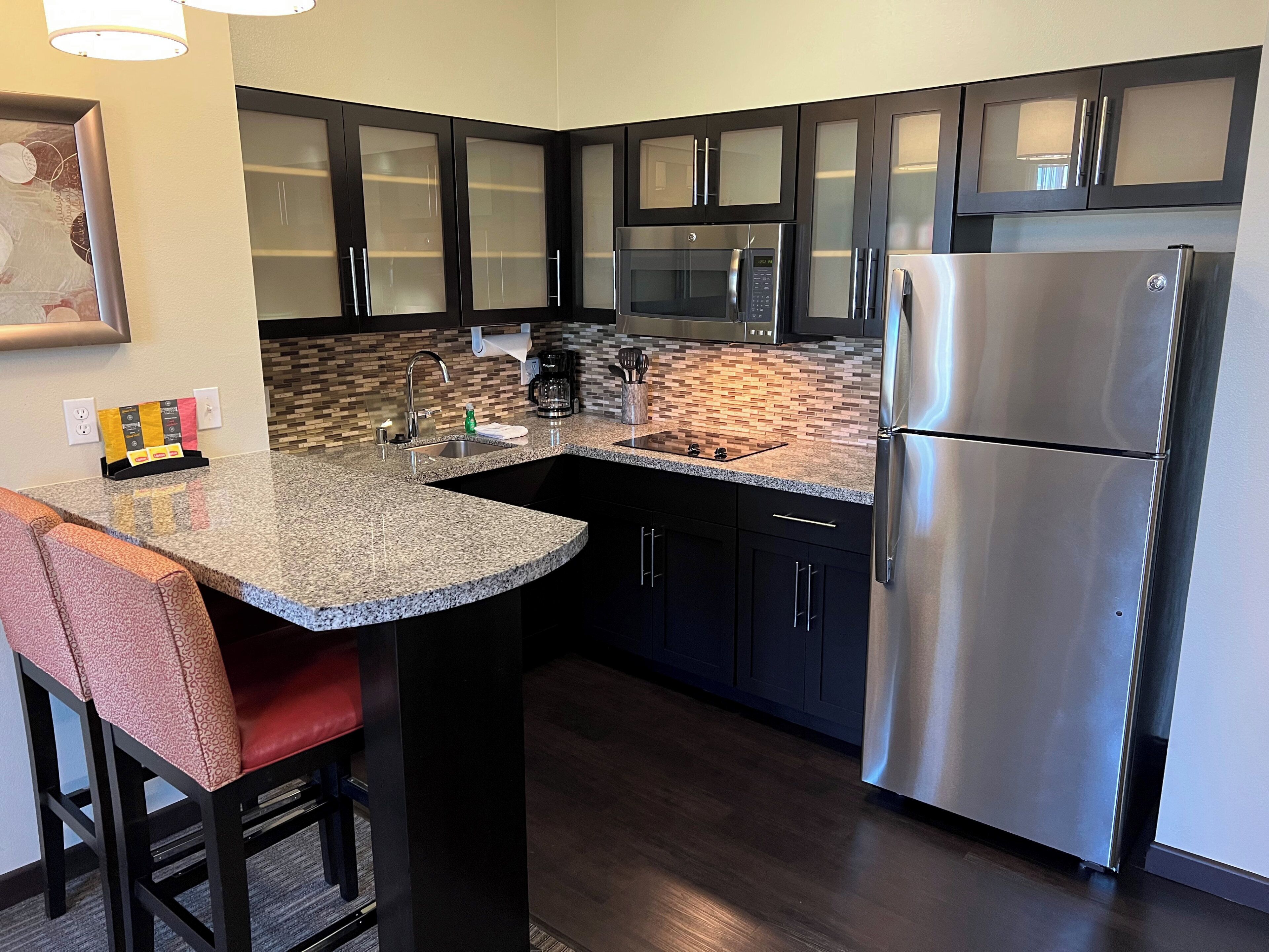 A modern kitchen with dark cabinets, a stainless steel refrigerator, and a granite countertop.