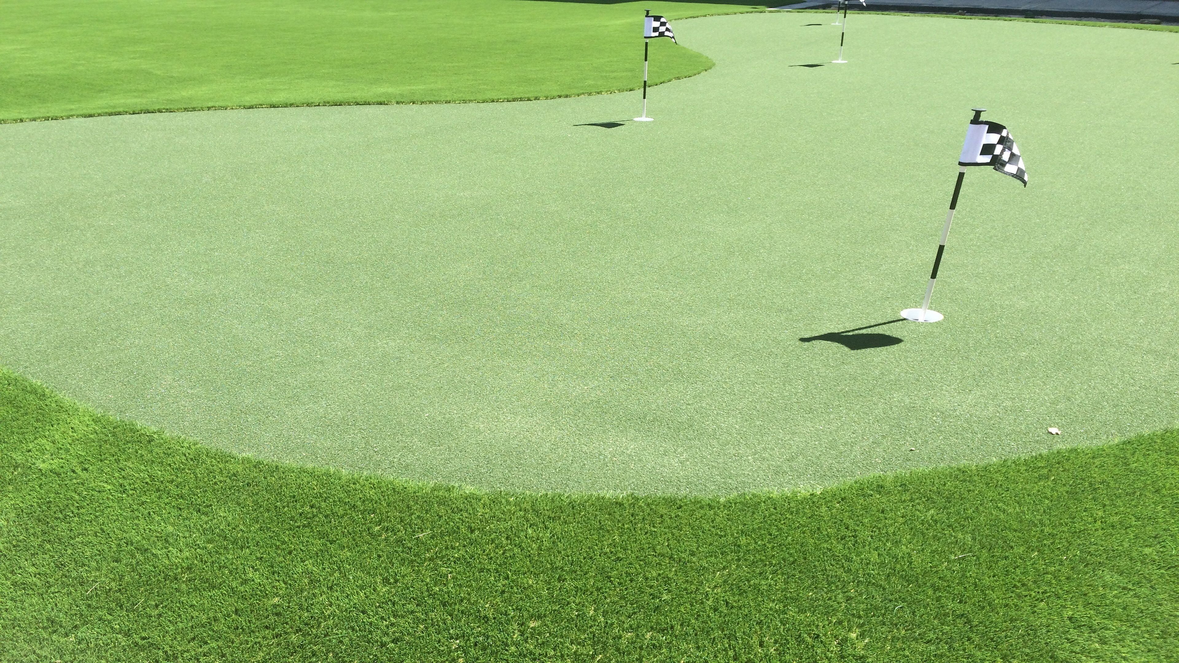 Un campo de golf con un putting green, banderas y un mástil de bandera.
