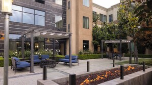 An outdoor seating area with modern furniture, a fire feature, and a building with large windows in the background. - Staybridge Suites Carlsbad by IHG (Carlsbad)