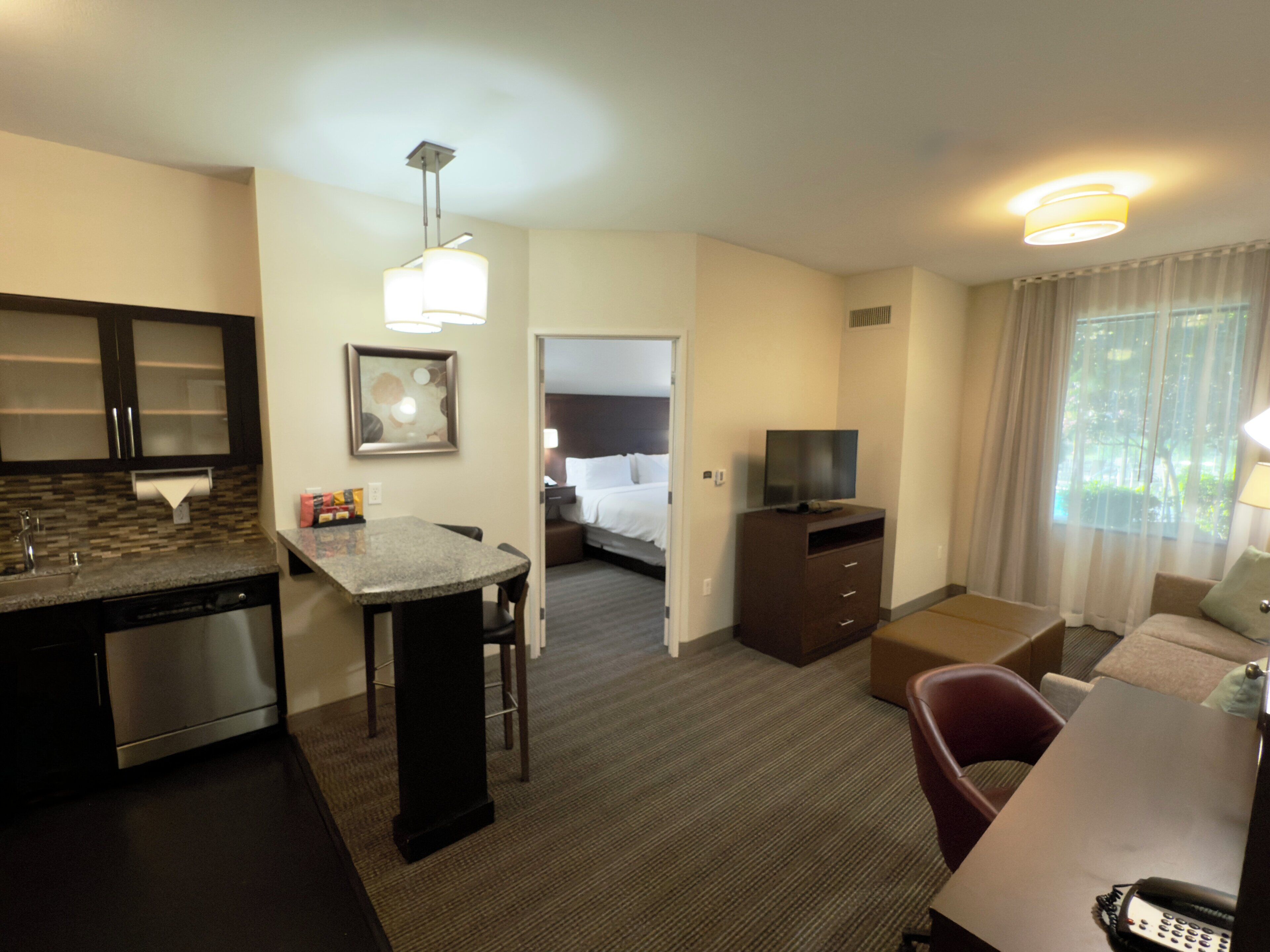 Ein Hotelzimmer mit Küchenzeile, Essbereich, Wohnbereich mit Fernseher und Schlafzimmer mit Bett und Fenster.