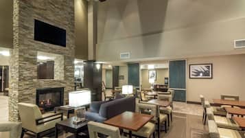 A spacious lobby with a stone fireplace, comfortable seating, and a flat-screen TV mounted on the wall.