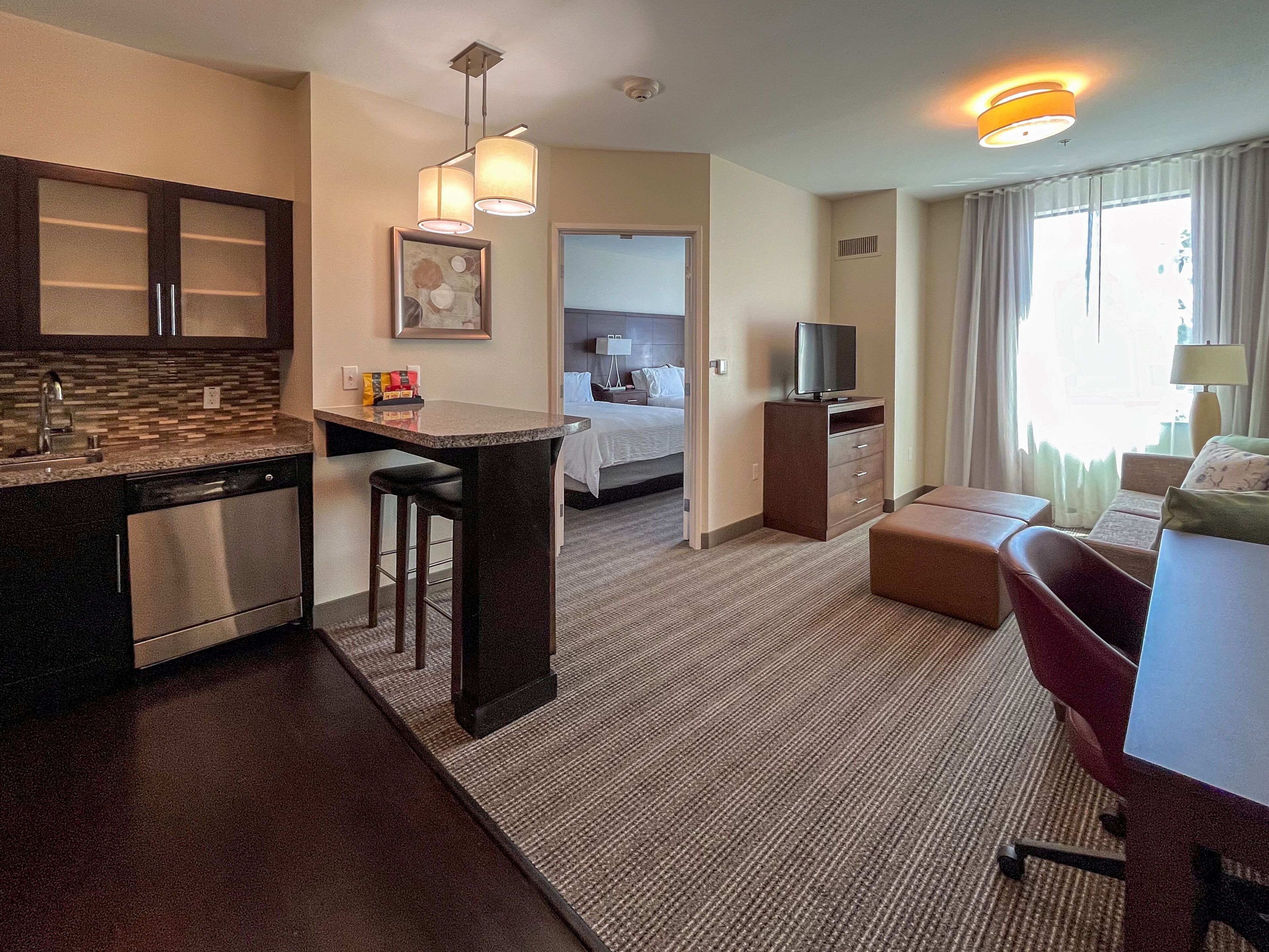 Habitación de hotel con kitchenette, cama, televisor y zona de estar.