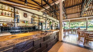 A bar area with wooden shelves stocked with bottles and glasses, a bar counter, and a dining area with wooden furniture. - Ocean Sun Dive Resort (Tulamben)