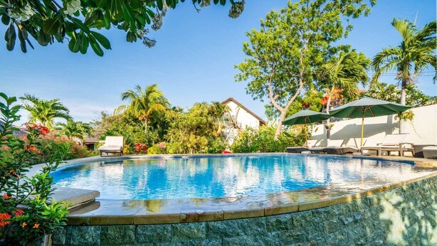 A swimming pool with a stone border, surrounded by lush greenery and a few lounge chairs. - Ocean Sun Dive Resort (Tulamben)